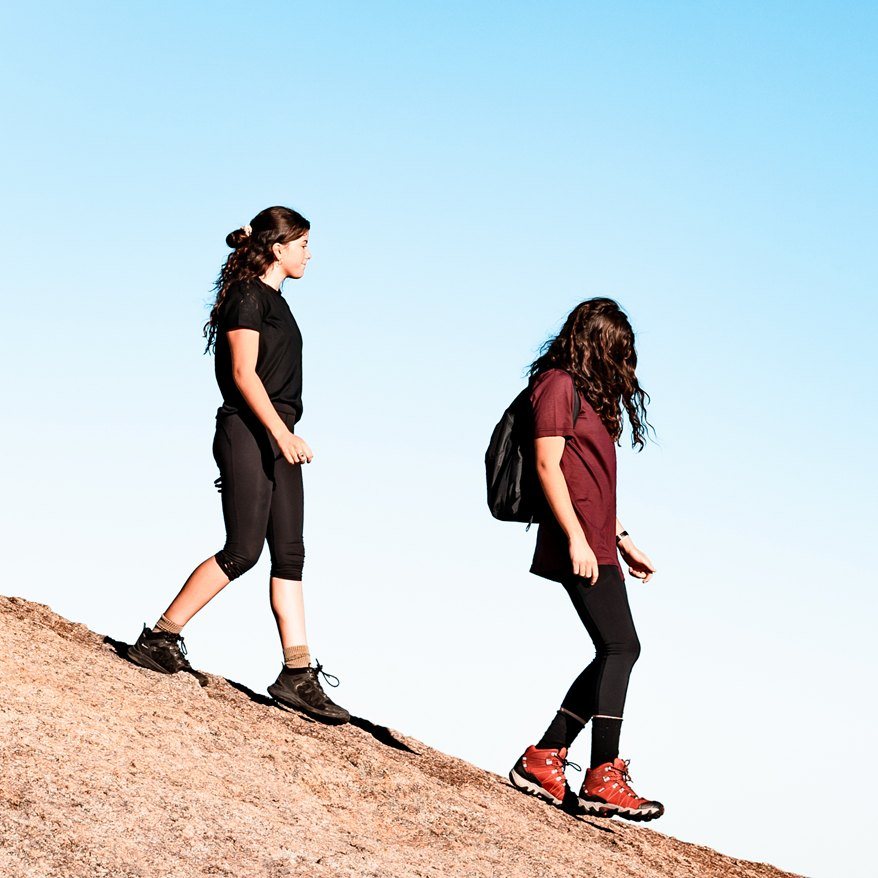 Two hikers in Black and Plum merino tees climbing a granite slope