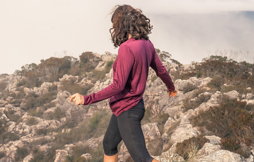 Hiker in a plum Ottie merino long sleeve walking over rocks
