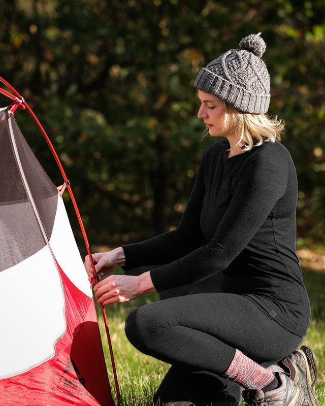 Hiker in black merino thermals pitching a tent