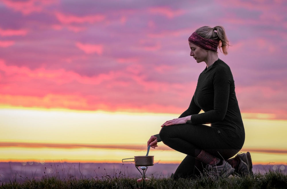 Hiker in black merino thermals cooking at sunset