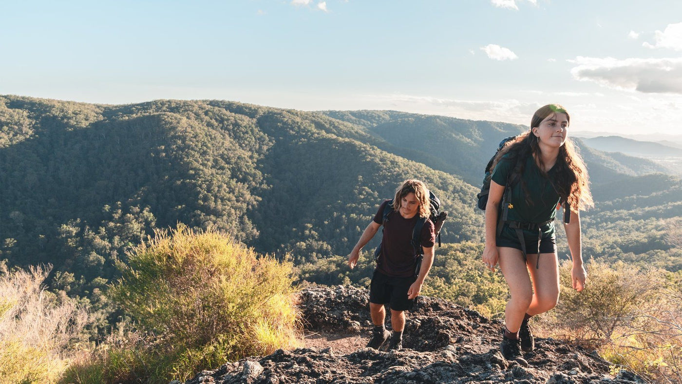 Two hikers with packs climbing a rocky ridge in Ottie merino tees